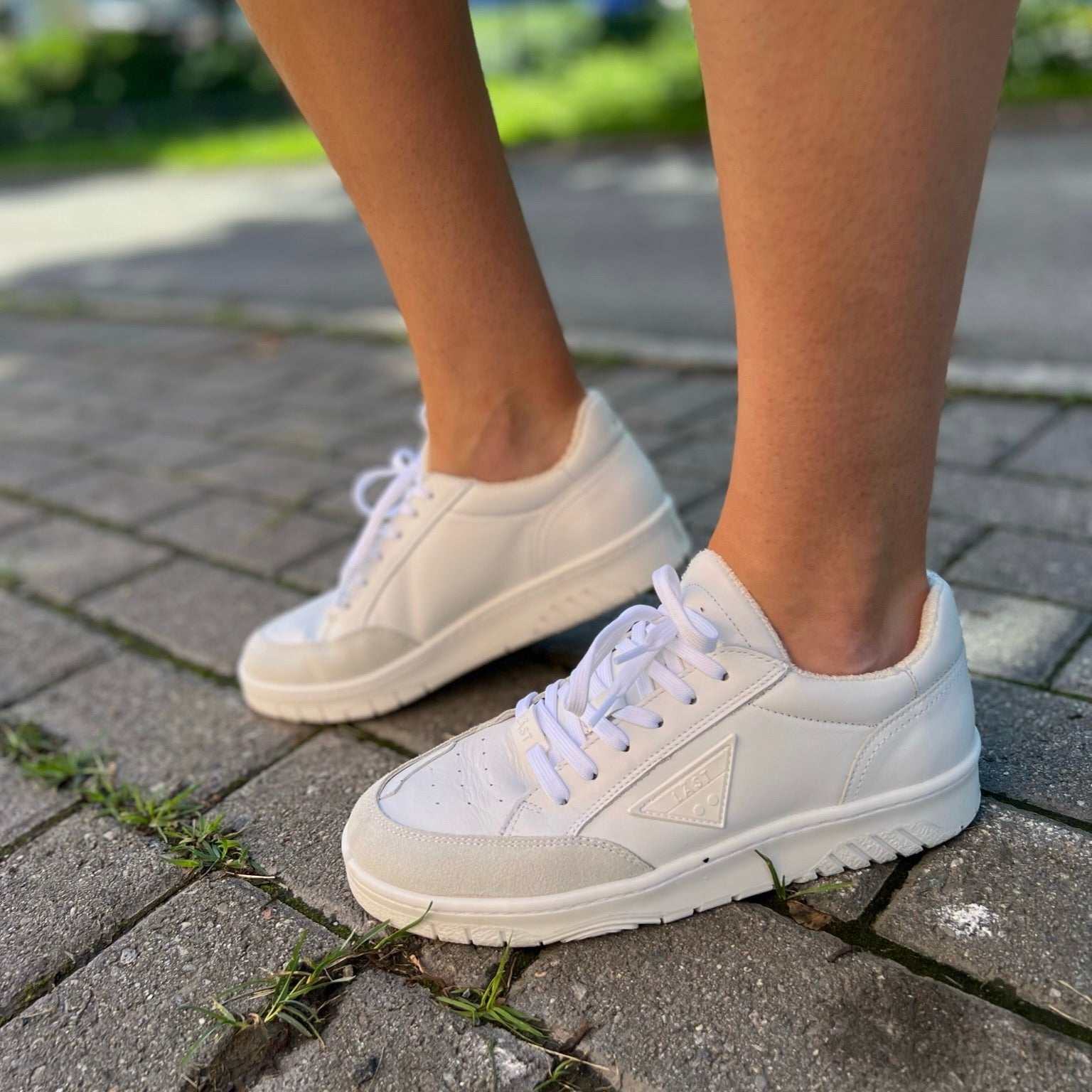 Header photo for the "Shoes" Collection-site, with a picture of white sneakers in vegan leather, outside on the asphalt